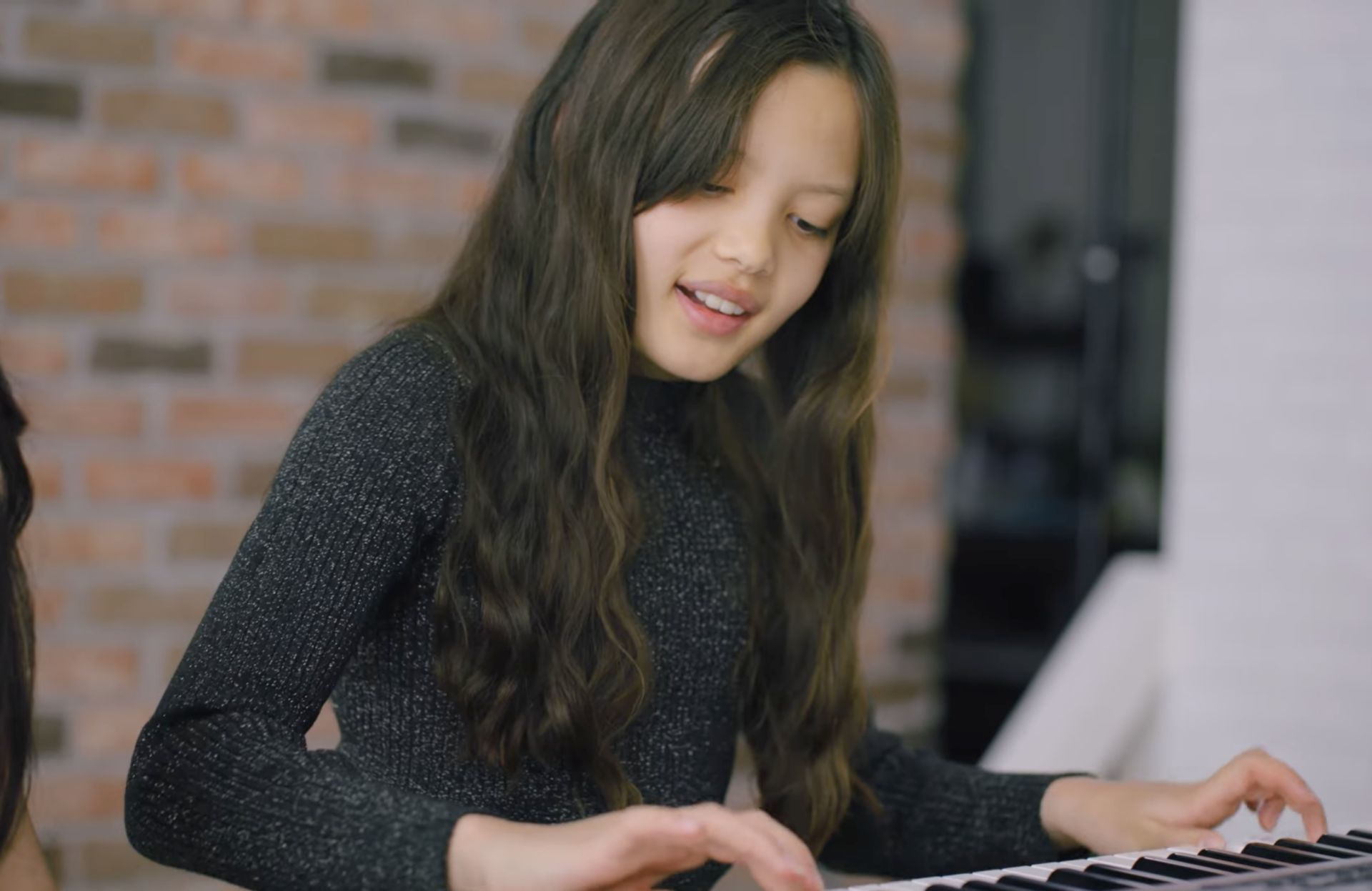 Girl playing piano with a gentle smile on her face.